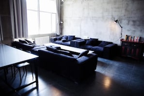 A modern living room with a sectional sofa, a dining table, and a bookshelf. - Hostel On The Way (Shayibake Urumqi)