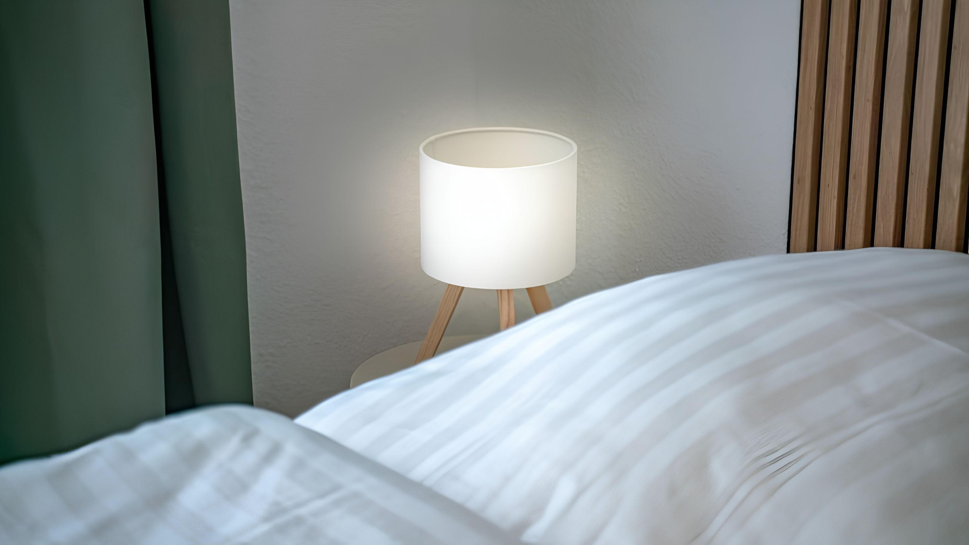 Un lit avec du linge de lit blanc et une lampe de chevet avec un abat-jour blanc.
