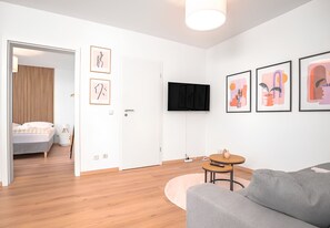 Un saló modern amb un sofà gris, una taula de centre rodona de fusta i un televisor pla penjat a la paret.
