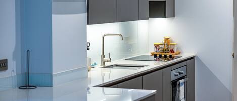 A modern kitchen with a stainless steel sink, a built-in oven, and a countertop with a glass backsplash.