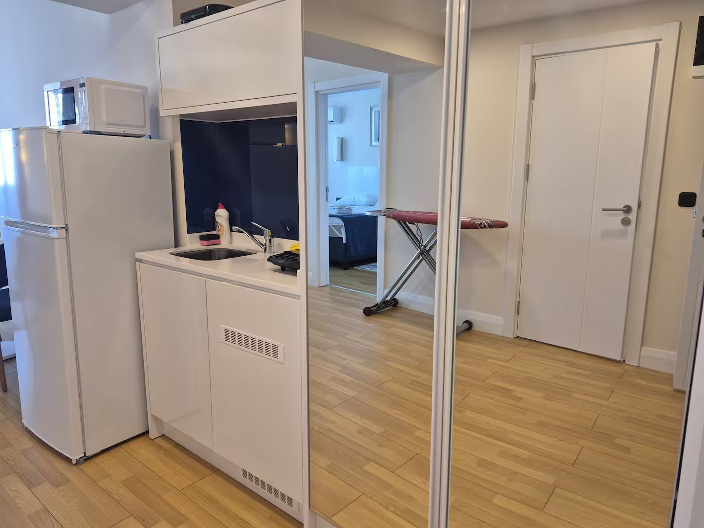 Eine kleine Küche mit Mikrowelle, Spüle und Bügelbrett.