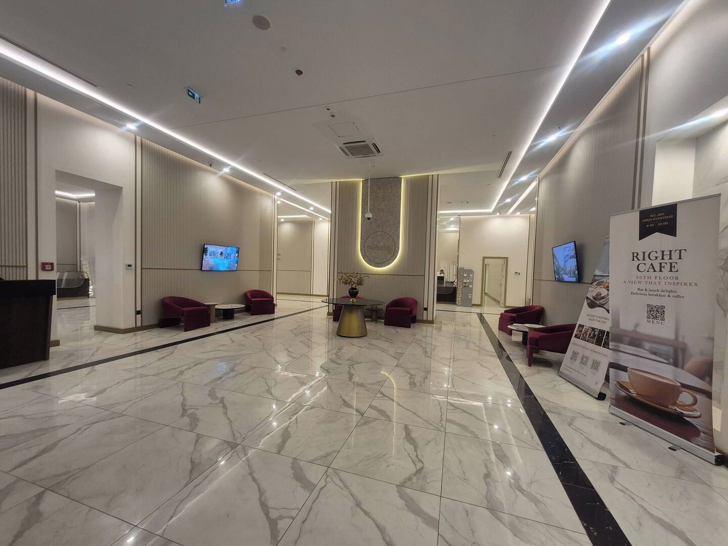 Un lobby moderno de hotel con piso de mármol, zonas de estar, un mostrador de recepción y un letrero de cafetería.