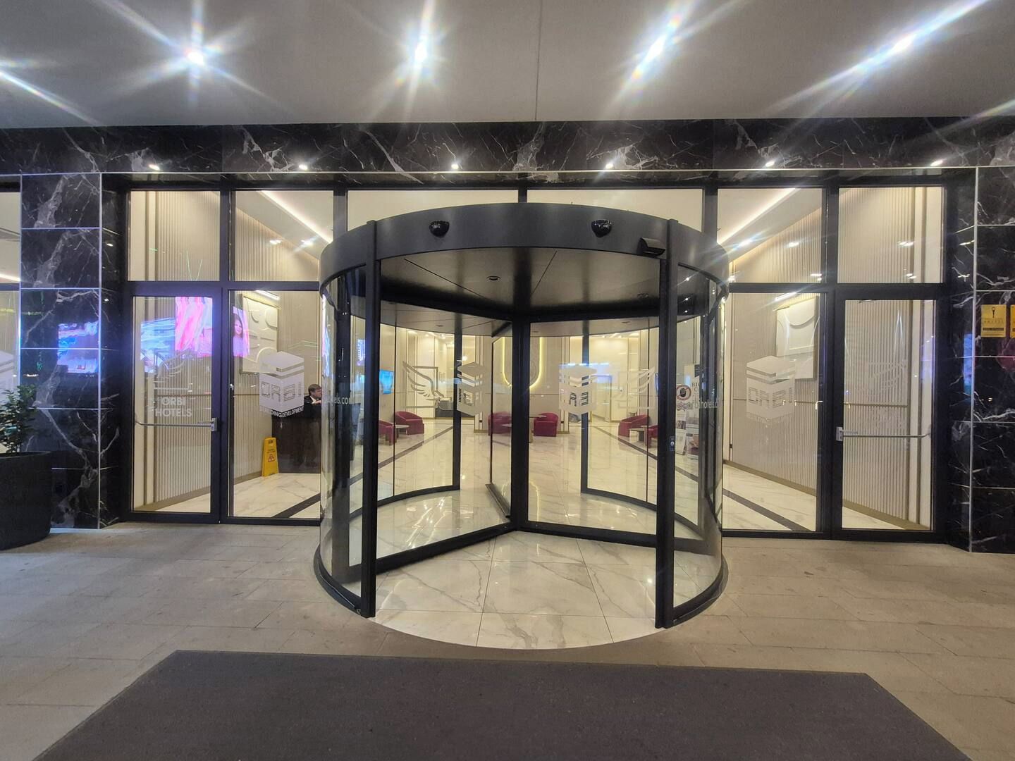 Entrada con puerta giratoria, paneles de vidrio y suelo de mármol.