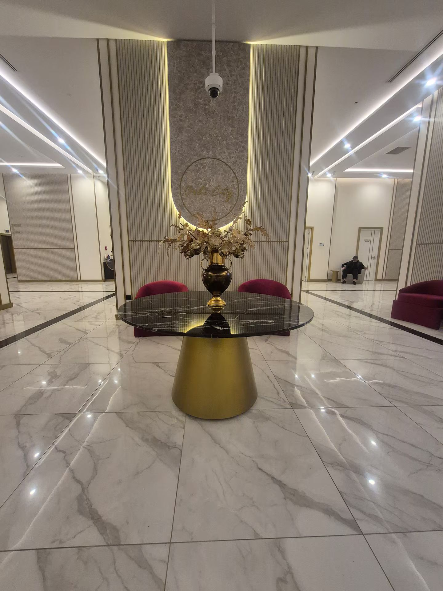 A modern lobby with a marble floor, a round table with a gold base, and red chairs.