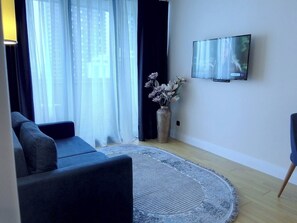 Ein modernes Wohnzimmer mit einer Couch, einem an der Wand montierten Fernseher und einer dekorativen Vase mit Blumen.
