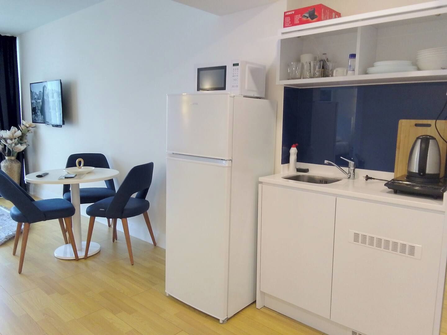 Une petite cuisine équipée d’un four à micro-ondes, d’un petit évier et d’une bouilloire. Un coin repas est aménagé avec une table ronde et deux chaises.