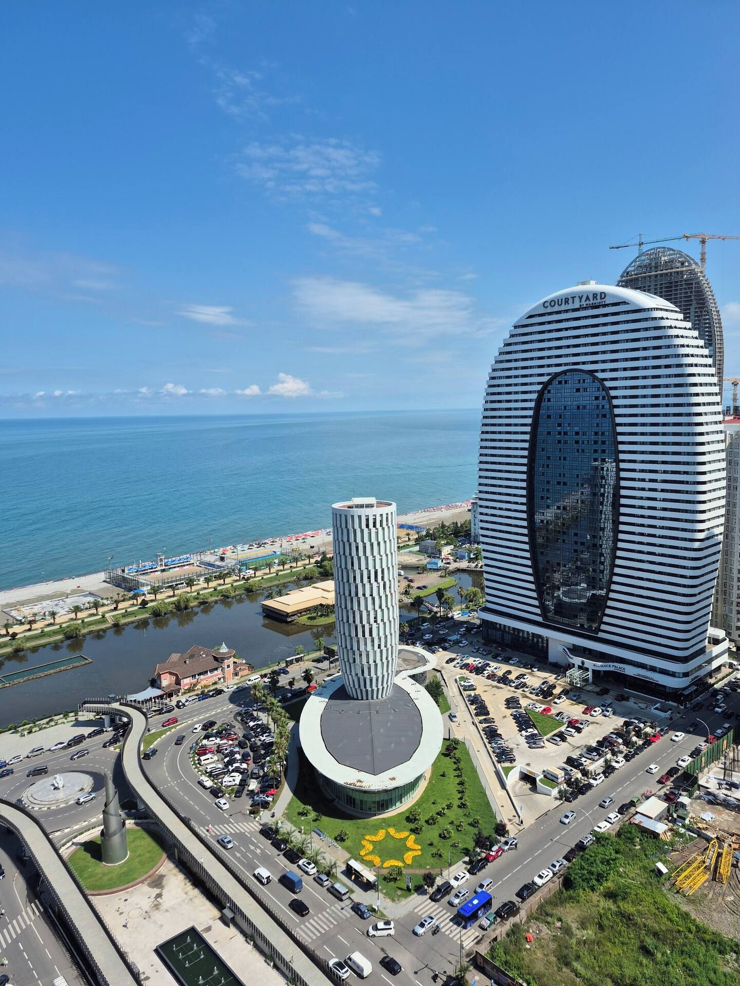 A modern hotel with a distinctive curved facade, a central cylindrical structure, and a view of the sea.