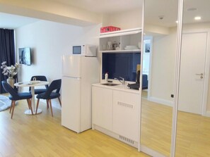 Eine kleine Küche mit Kühlschrank, Mikrowelle und Spüle. Ein Essbereich mit zwei Stühlen und einem Tisch ist ebenfalls vorhanden.