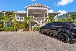 A building with a covered entrance, a staircase, and a car parked in front. - Ground-Floor 1BR, Marina View, Sleeps 3 · Apt 22 Ocean Breeze (Kralendijk)