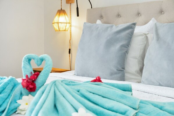 Een netjes opgemaakt bed met een handdoek in de vorm van een hart, een bedlampje en een gestuikt hoofdbord.