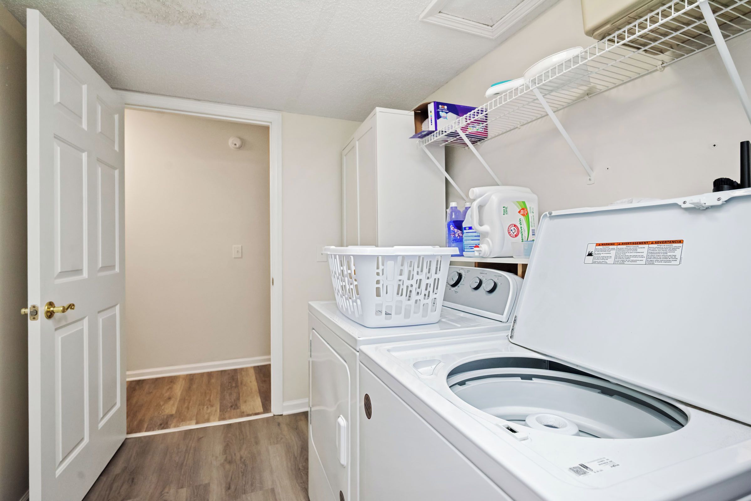 Een wasserette met een voorlader wasmachine, een witte wasmand en een plank met schoonmaakmiddelen.