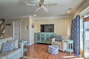 A living room with a ceiling fan, a television on a cabinet, a sofa, an ottoman, and a patterned throw pillow. - Walk to Beach:  Waterfront Condo in Ocean City! (Ocean City)