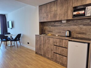 Una cocina compacta con armarios de madera, microondas, hervidor y un refrigerador pequeño.
