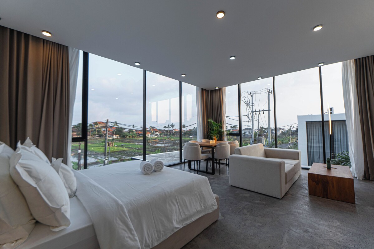 A modern hotel room with a large bed, a seating area with a table, and a view of the cityscape.