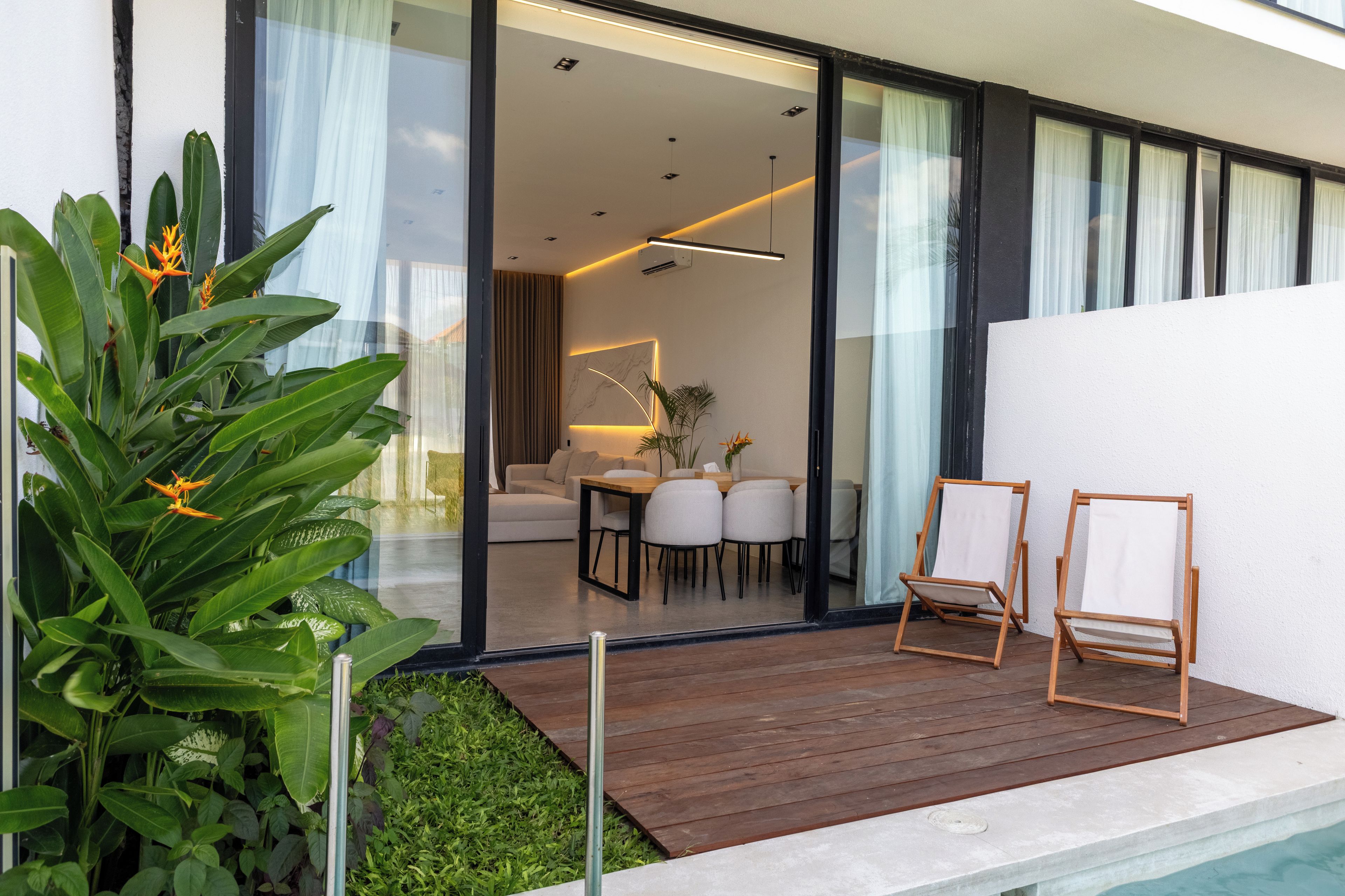 Ein modernes Haus mit Glastür, die zu einem Wohnbereich, einer Holzterrasse und einem kleinen Pool führt.