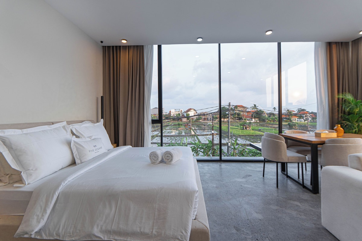 A hotel room with a bed, a desk, and a view of a cityscape.