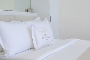 A bed with white bedding and pillows, a shelf above the bed, and a door to the right. - Five Oceans Residence Berawa (Kec. Kuta Utara, Kab. Badung)