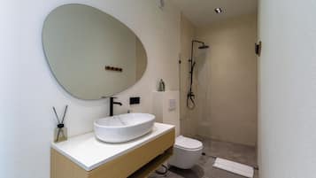 A modern bathroom with a round mirror, white sink, and a shower area.