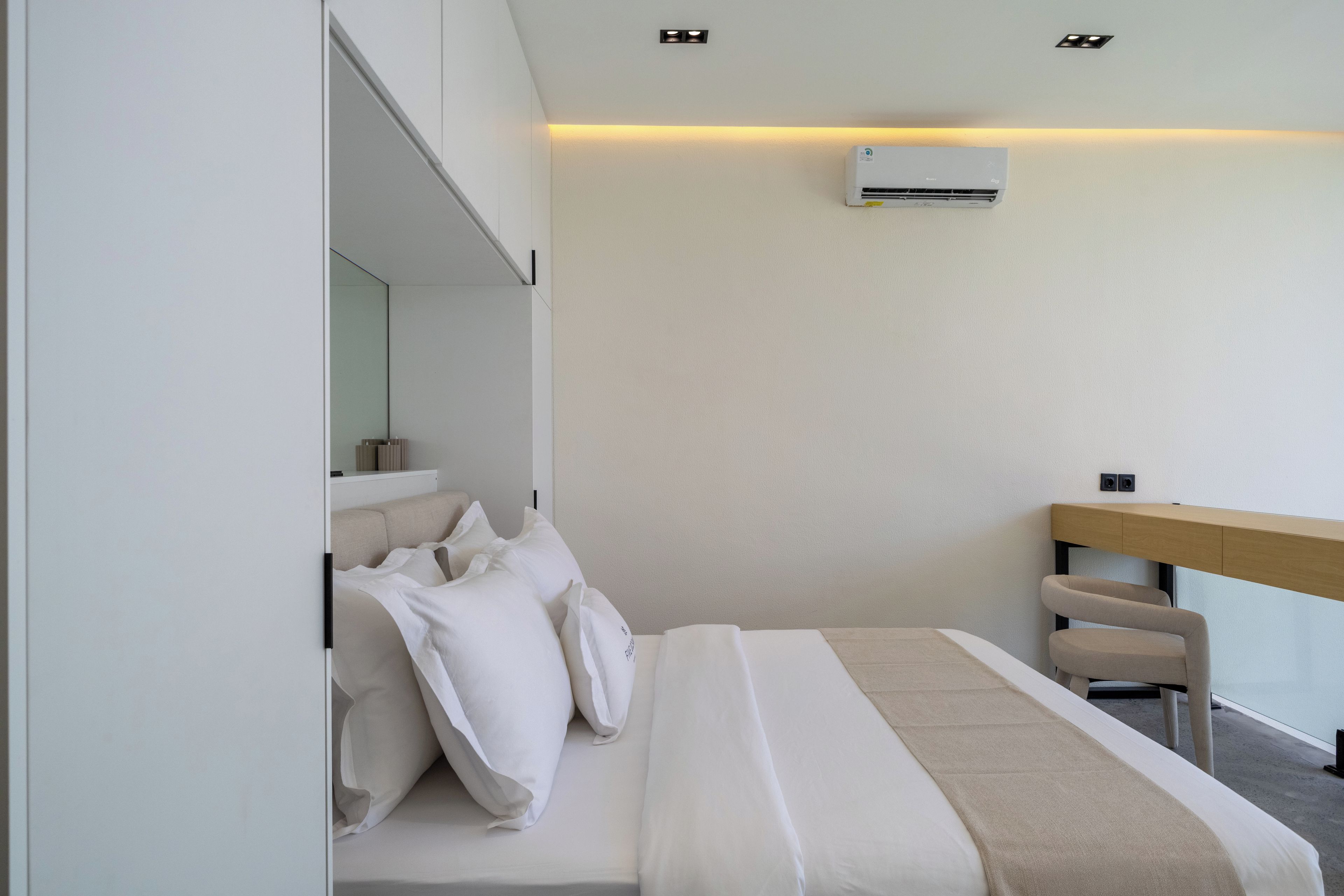 A modern hotel room with a bed, a desk, and an air conditioning unit on the wall.