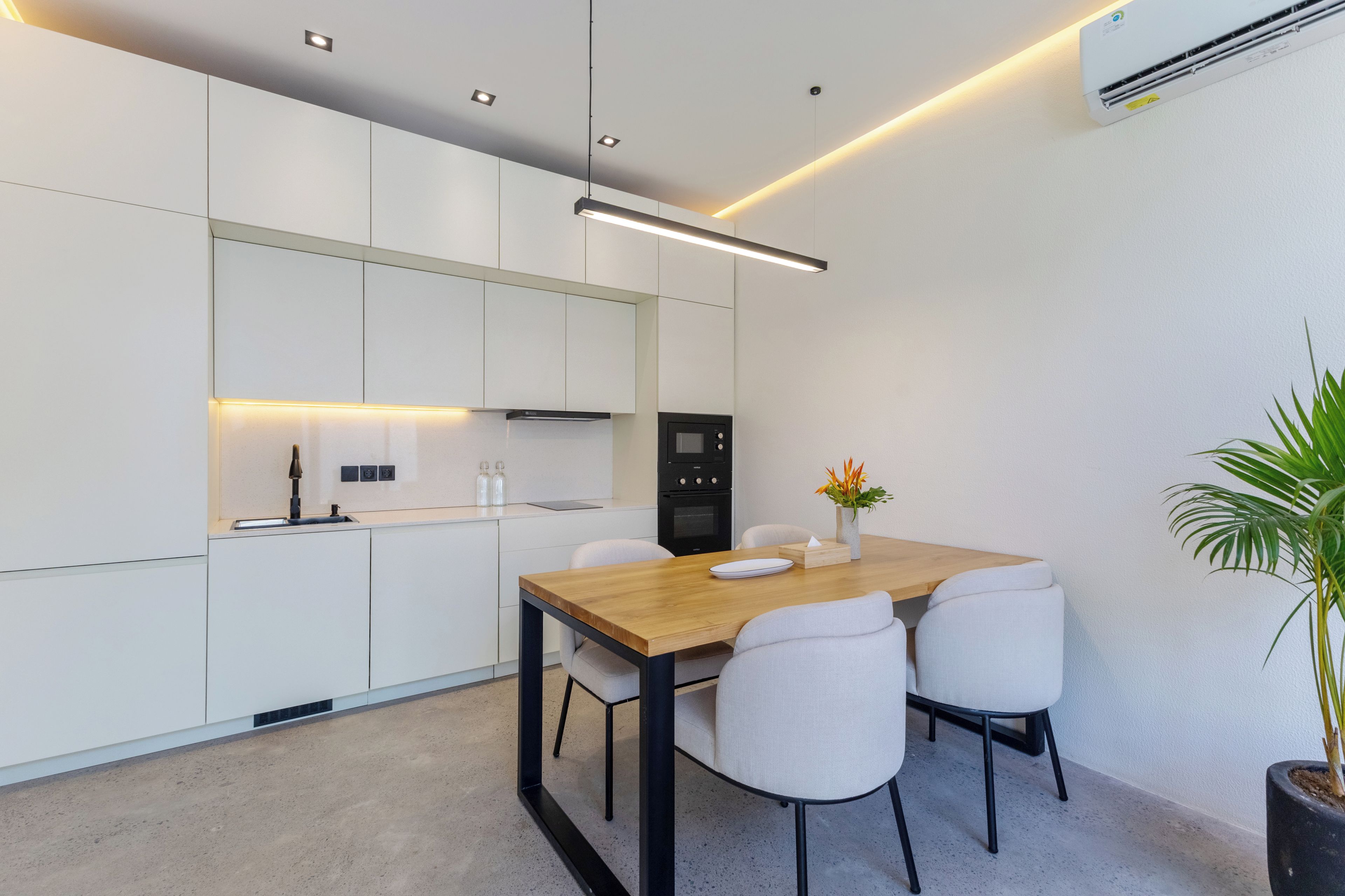 A modern kitchen with white cabinets, a wooden dining table, and a black refrigerator.