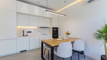 A modern kitchen with white cabinets, a wooden dining table, and a black refrigerator.