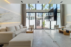 A modern living room with a sofa, armchairs, a coffee table, and a TV. - Five Oceans Residence Berawa (Kec. Kuta Utara, Kab. Badung)