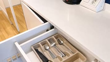 A kitchen area with a white countertop, a kettle, and a drawer containing utensils.