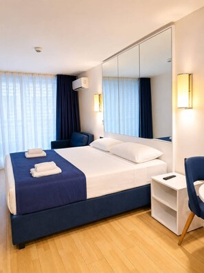 Habitación de hotel con una cama grande, un escritorio, una silla, un espejo y un equipo de aire acondicionado.