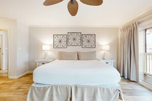 Une chambre à coucher avec un grand lit, deux tables de chevet avec des lampes, un ventilateur de plafond et trois panneaux décoratifs fixés au mur.