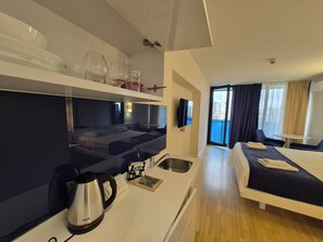 A hotel room with a bed, a desk with a kettle, a TV, and a balcony with curtains. - ORBI D2 "14 " Seaview quite studio (Batumi)