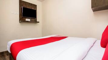 A hotel room with a bed, a mounted television, and a wall-mounted shelf.
