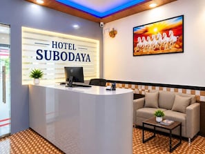A hotel reception desk with a computer, a sofa, and a coffee table. - Classic Hotel Subodaya (Navi Mumbai)