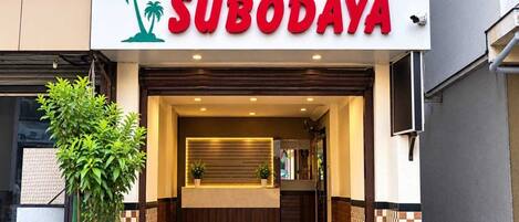 A hotel entrance with a reception desk, a palm tree logo, and a sign that reads 'HOTEL SUBODAYA.'