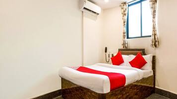 Una habitación de hotel con cama, teléfono, equipo de aire acondicionado y ventana con cortinas.