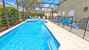 A swimming pool with a clear blue water feature, surrounded by a covered patio area with chairs and a fence. - Our Happy Place • Disney Charm, Private Pool & Spa (Kissimmee)