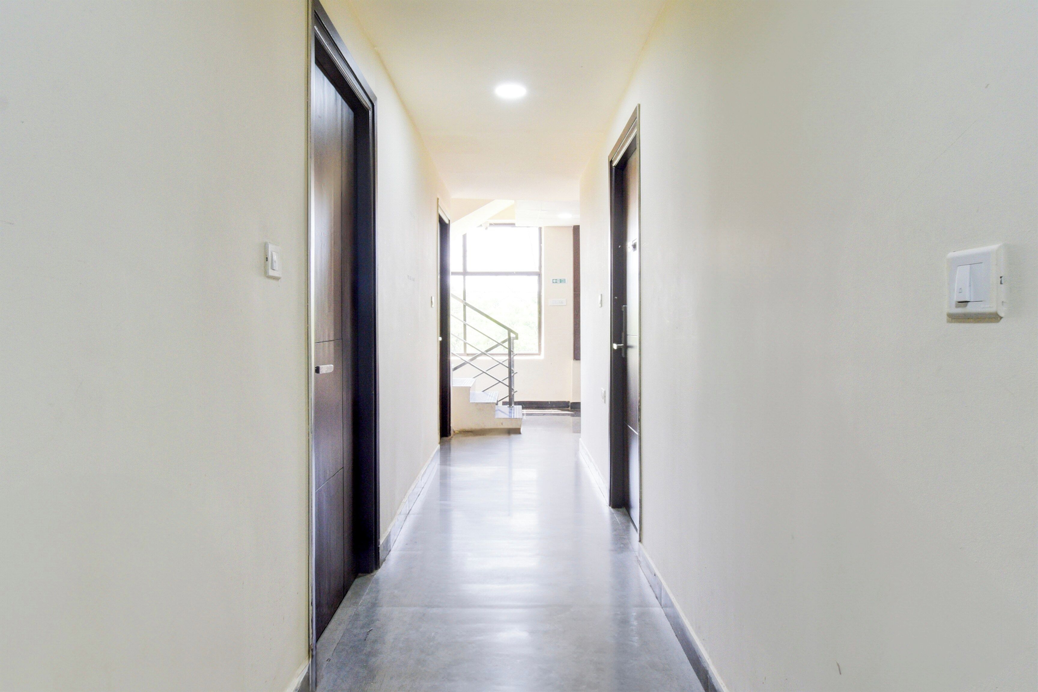 Un pasillo con puertas a ambos lados, una escalera al final e interruptor de luz en la pared.