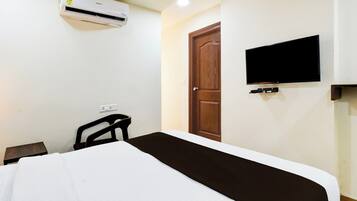 Een hotelkamer met een bed, een aan de muur bevestigde televisie en een airconditioning boven het bed.