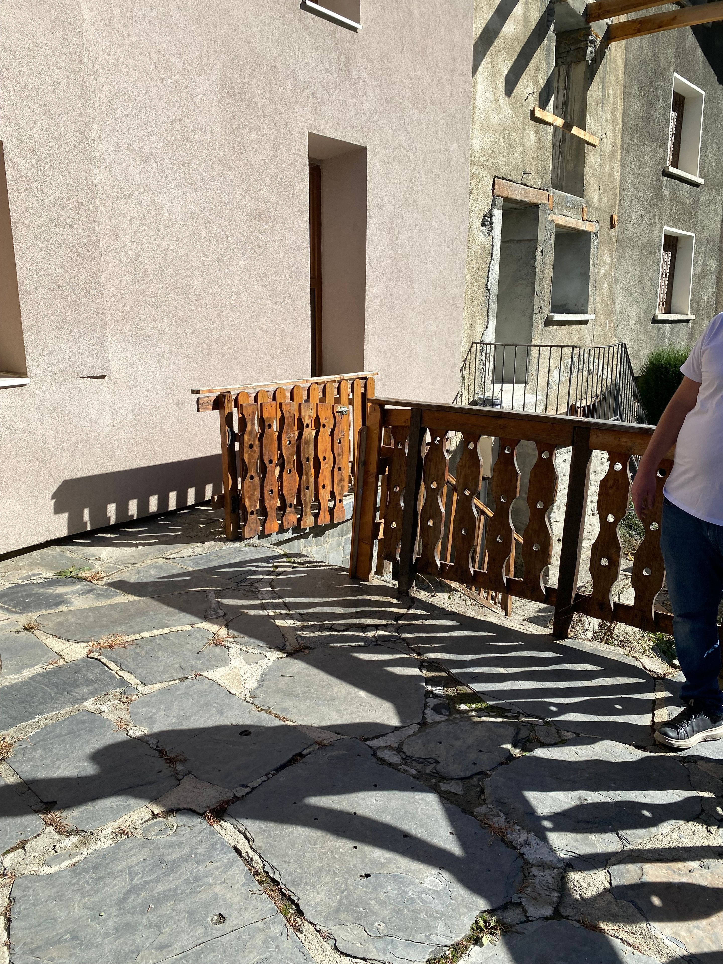 Ein mit Steinplatten belegter Innenhof mit Holzzaun, einem Hauseingang und einer Treppe, die zu einer oberen Ebene führt.
