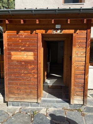 Une entrée en bois avec une pancarte indiquant « MAISON », des marches en pierre et un paillasson.