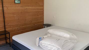 Ein Schlafzimmer mit einer Holzwand, einem Bett mit Matratze und Kissen, einem kleinen Tisch und einem Bild an der Wand.