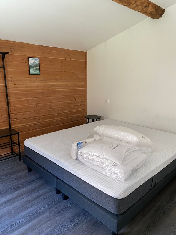 Une chambre avec un mur en bois, un lit avec un matelas et des oreillers, une petite table et un tableau accroché au mur.