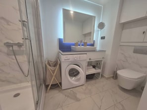 Et moderne badeværelse med en glasafskærmet bruseniche, indbygget vaskemaskine og toilet.
