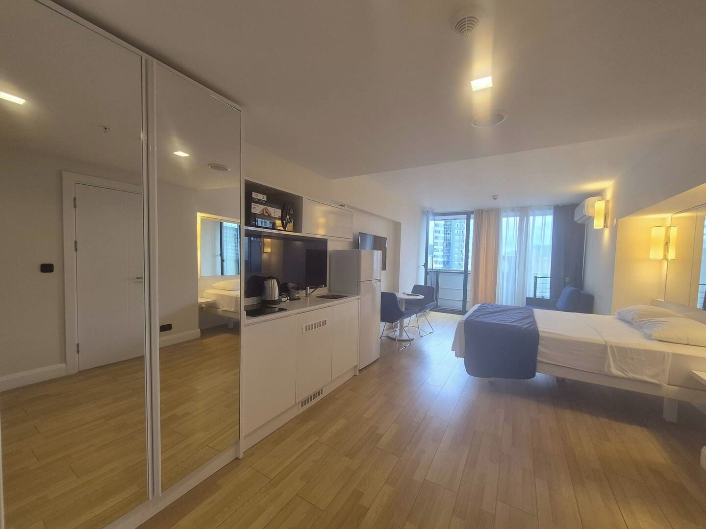 Une chambre d’hôtel moderne équipée d’un lit, d’un bureau, d’une kitchenette et d’un placard avec porte coulissante.
