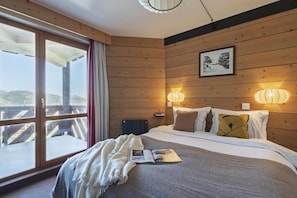 A hotel room with a bed, a window with curtains, a wall-mounted lamp, and a framed picture. - Wifi, 10m from ski slopes, balcony, ski locker, 75m², Val Thorens (Val Thorens)