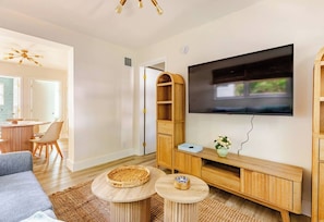 Una sala moderna con un televisor de pantalla plana, muebles de madera y un comedor al fondo.