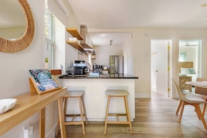 Una cocina moderna con una isla central, taburetes de bar y un comedor con mesa y sillas.