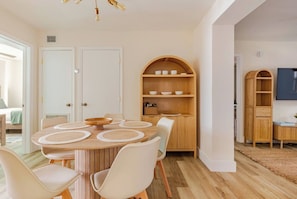 Un comedor con una mesa redonda, sillas blancas y un aparador de madera con estantes.