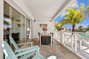 A balcony with a table and chairs, a view of the ocean, and a palm tree. - Ground-Floor Corner 1BR, Sleeps 4 · Apt 23 Ocean Breeze (Kralendijk)