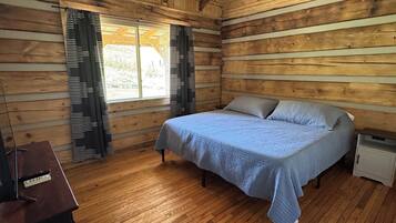 Un dormitorio de cabaña de madera con cama, cortinas, ventilador de techo y piso de madera.