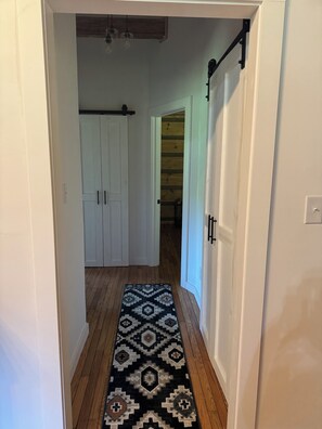 Un passadís amb una catifa estampada, terres de fusta, portes blanques i una làmpada al sostre.